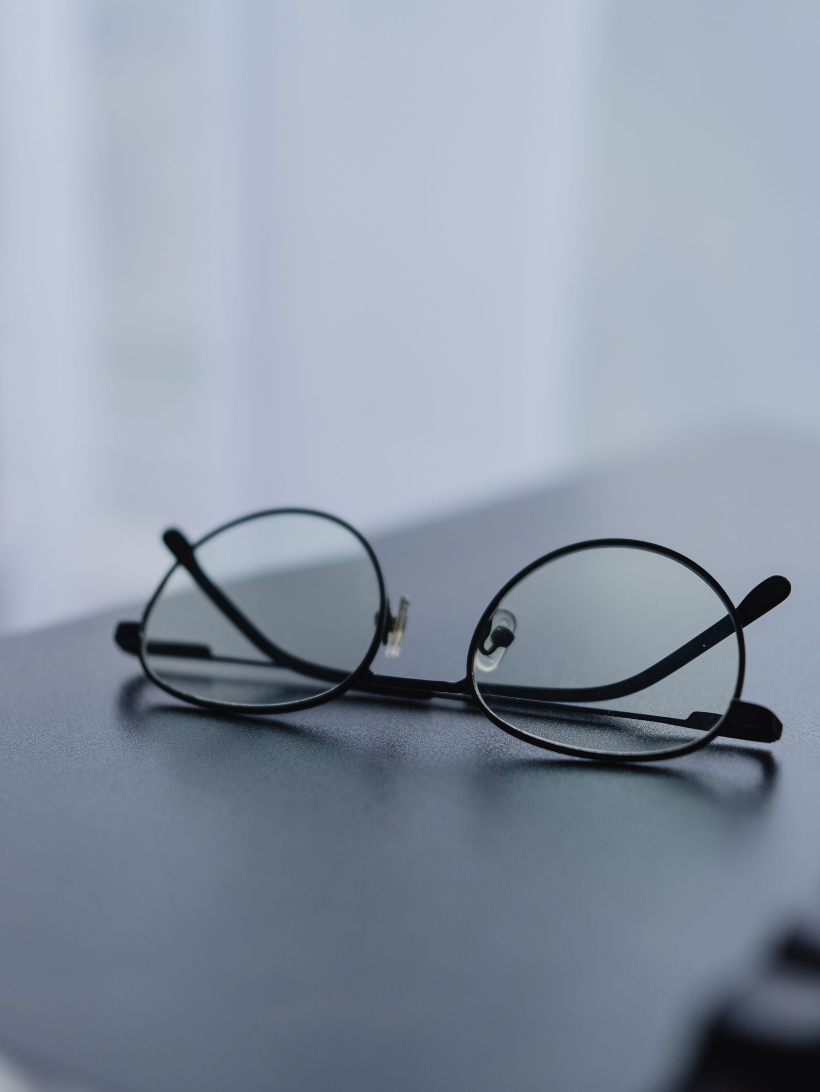 Óculos redondos de grau sobre mesa, com luz difusa e fundo desfocado.